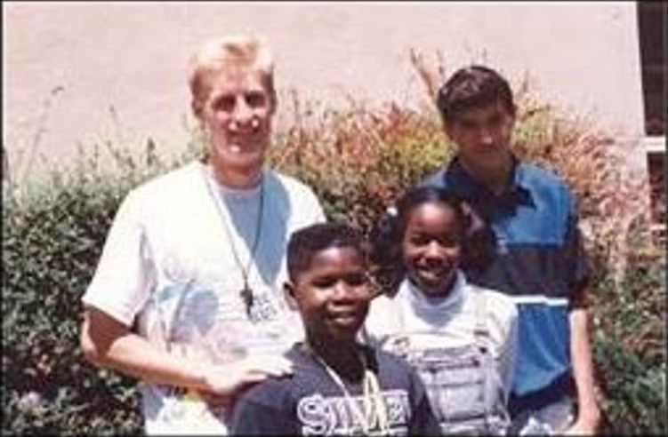 Two adults with a boy and a girl outdoors in front of bushes