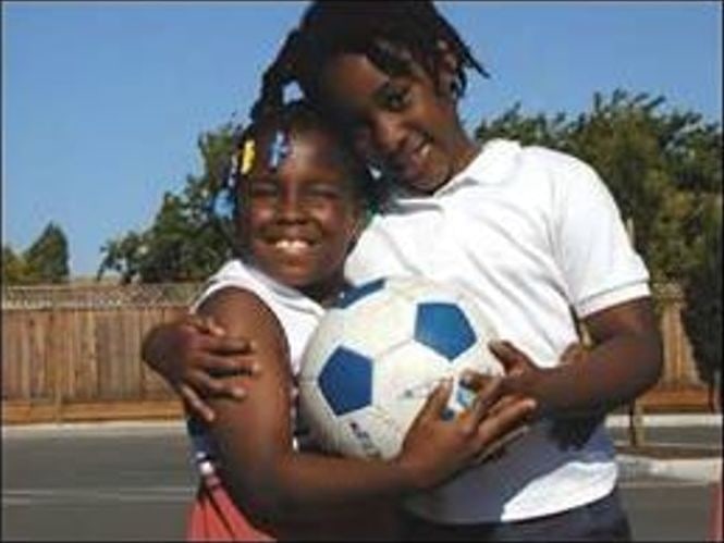Two girls outdoors hugging and holding a soccer ball