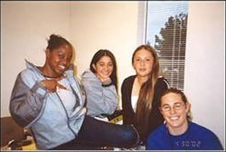 Four young people smiling indoors, one making a peace sign