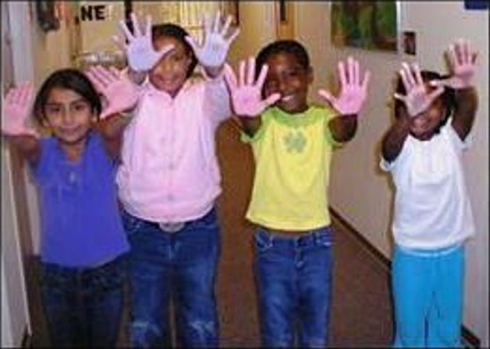 Children in a hallway holding up paint-covered hands