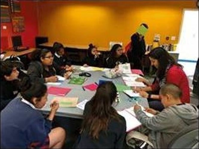 Students and an instructor gathered around a table with notebooks