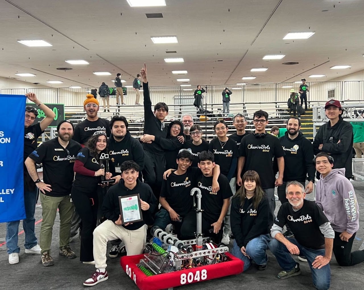 The Churrobots and their mentors gathered around their robot, one student holding an award, at the 2024 Silicon Valley Regional