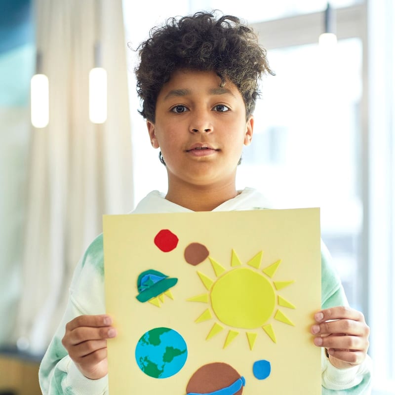 A student holding up a painting of the sun that they made