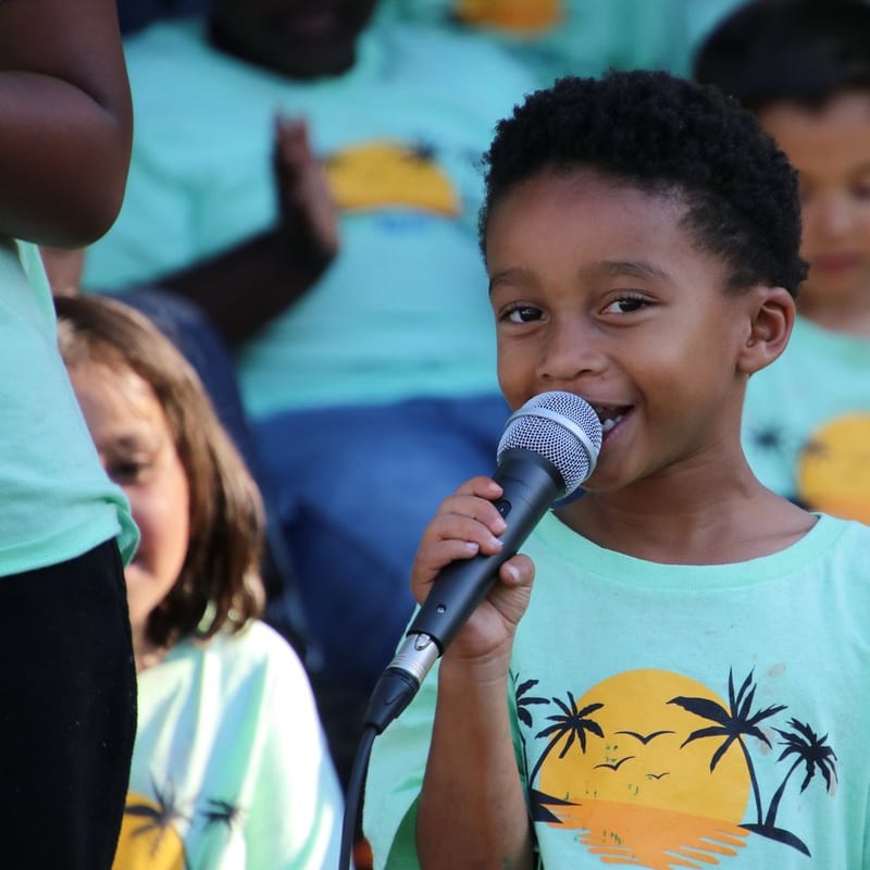 A child singing into a microphone at summer camp