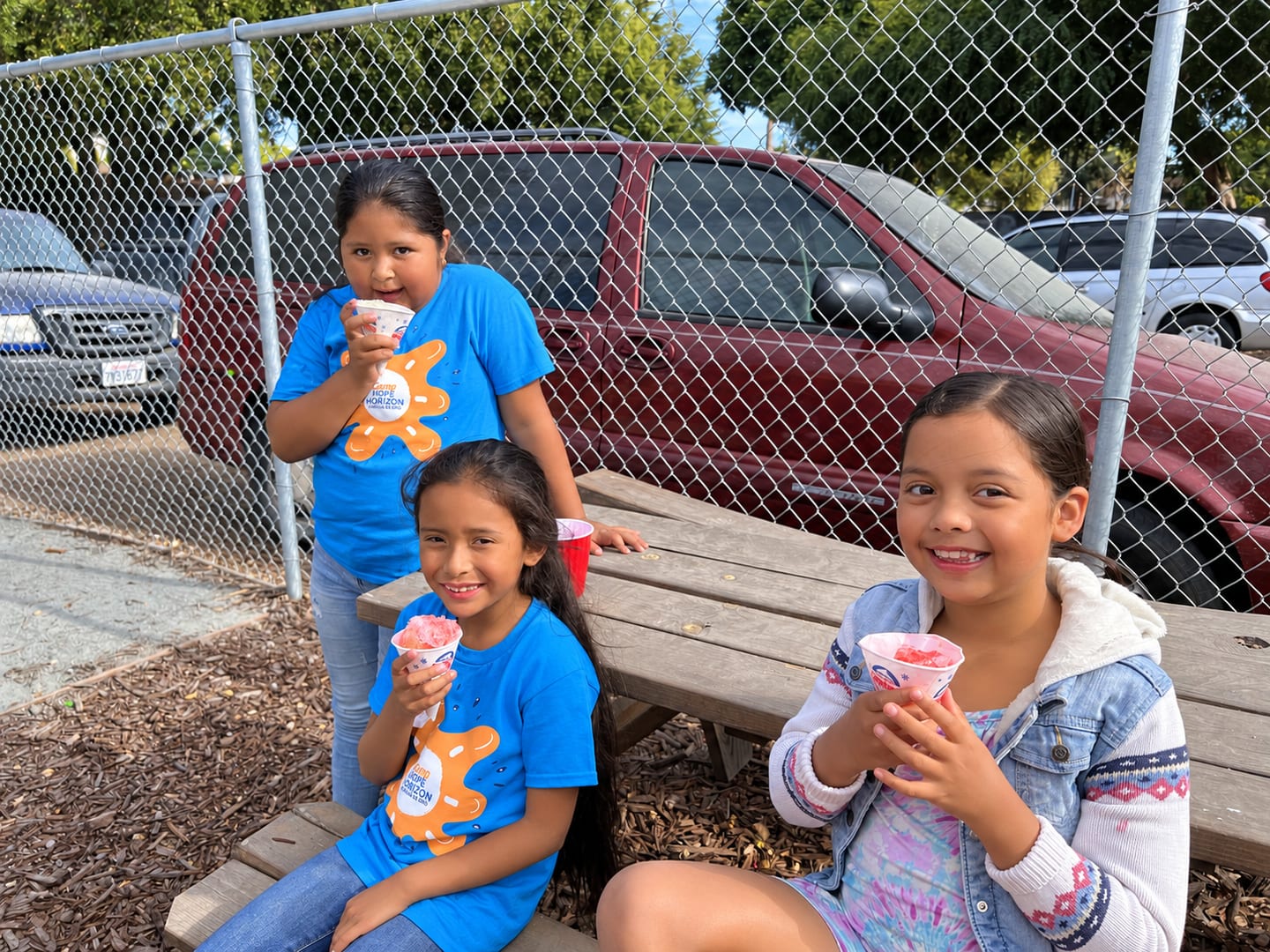 Three campers eating shaved ice at a picnic table, two of them in blue Hope Horizon shirts