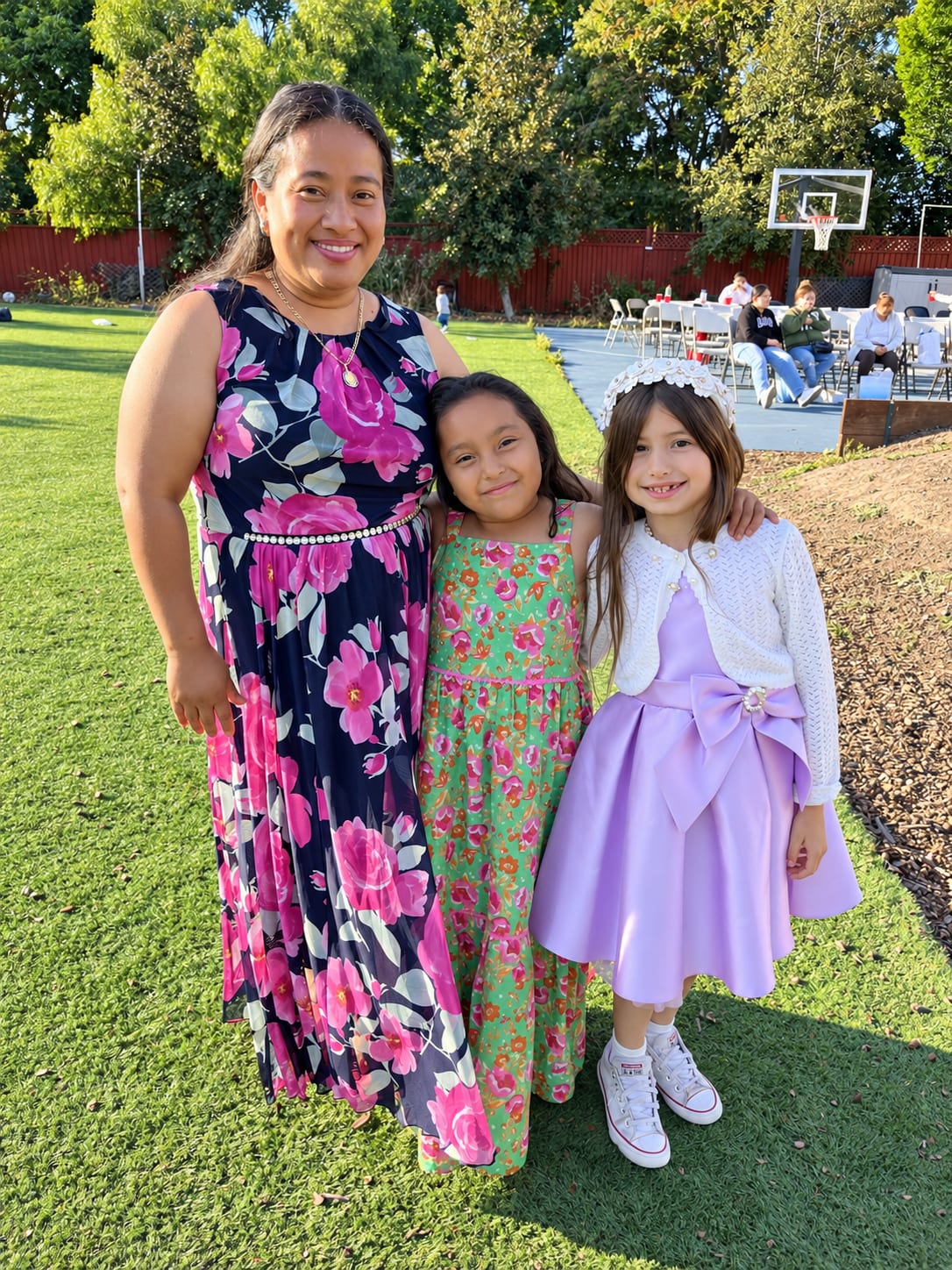 A woman standing with two girls in dresses on a lawn
