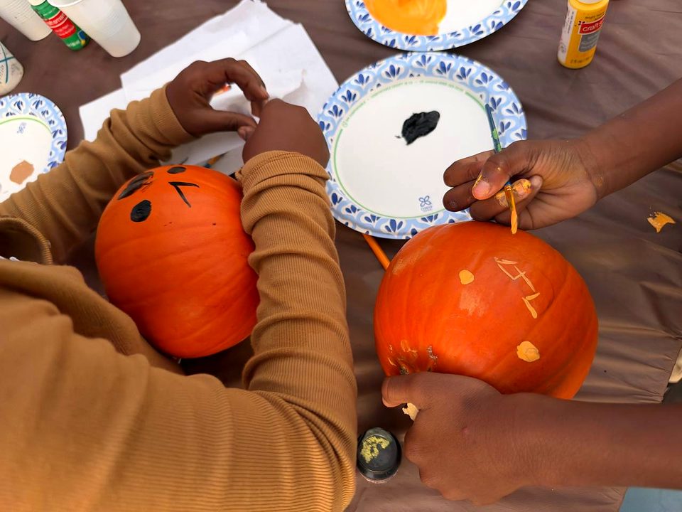 Two pairs of hands paint pumpkins at a table set with paint plates