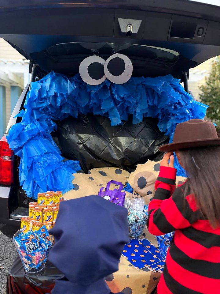 A car trunk decorated as a fuzzy blue monster with googly eyes, with snacks and treat bags in front