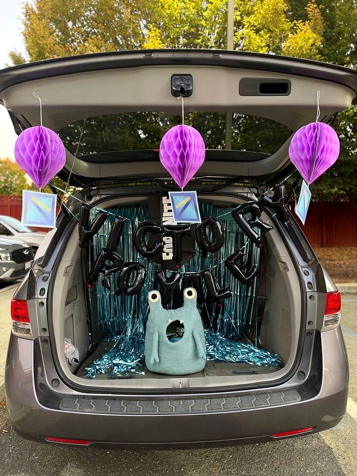 A minivan trunk with purple paper lanterns, teal tinsel and black balloon letters spelling Victory Royale