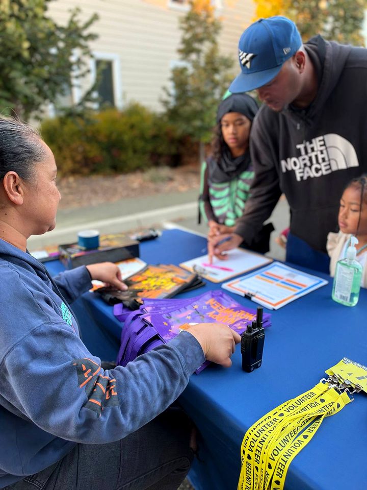 A volunteer at the welcome table helps a family sign in while children wait nearby
