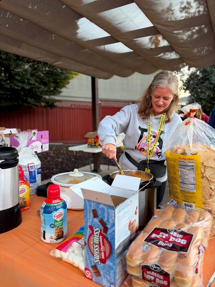 A volunteer wearing a yellow lanyard ladles food from a slow cooker at the food table