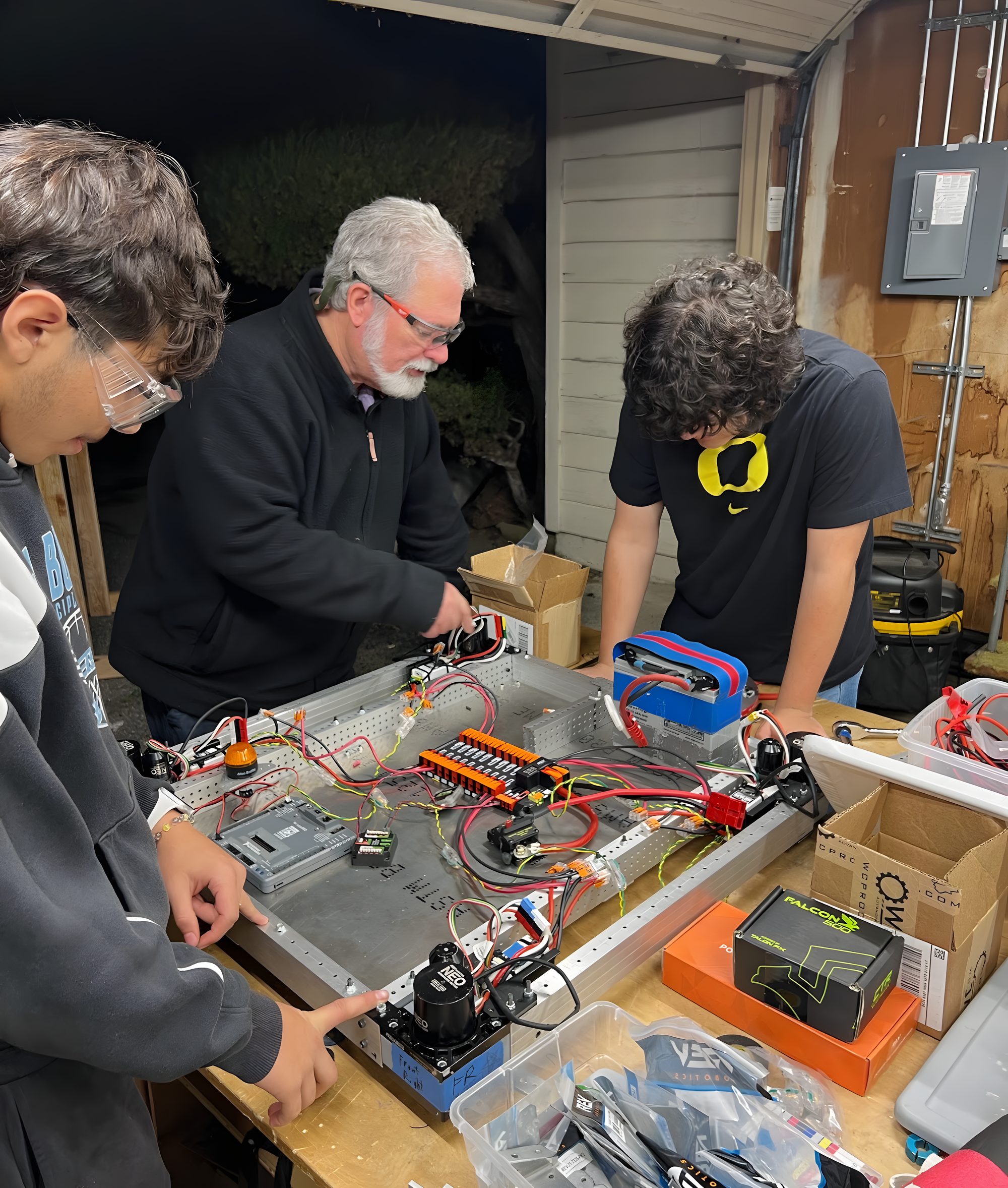 A mentor and two students wire the electrical board on a robot chassis