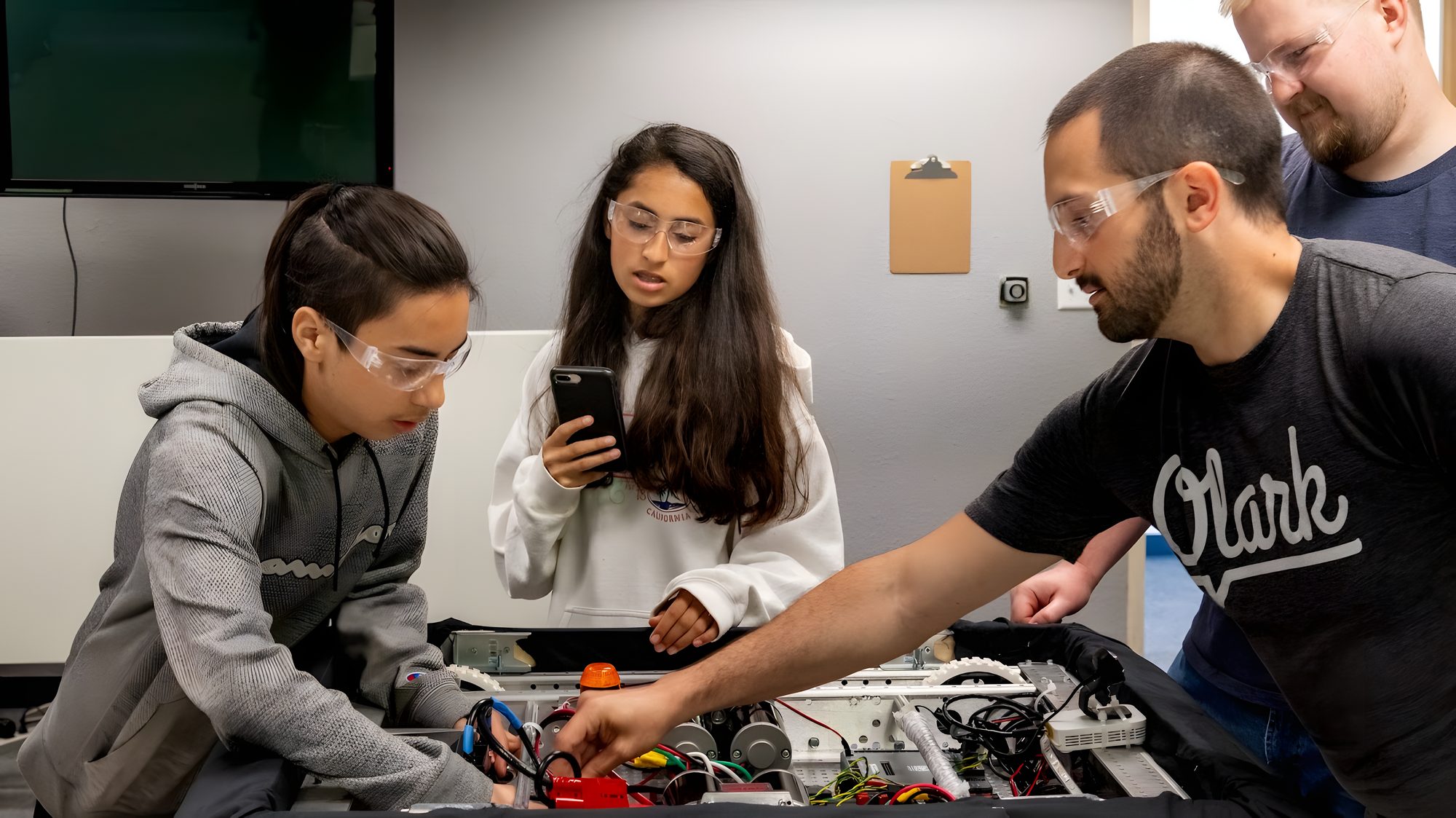 A mentor works with two students on a robot chassis in the workshop