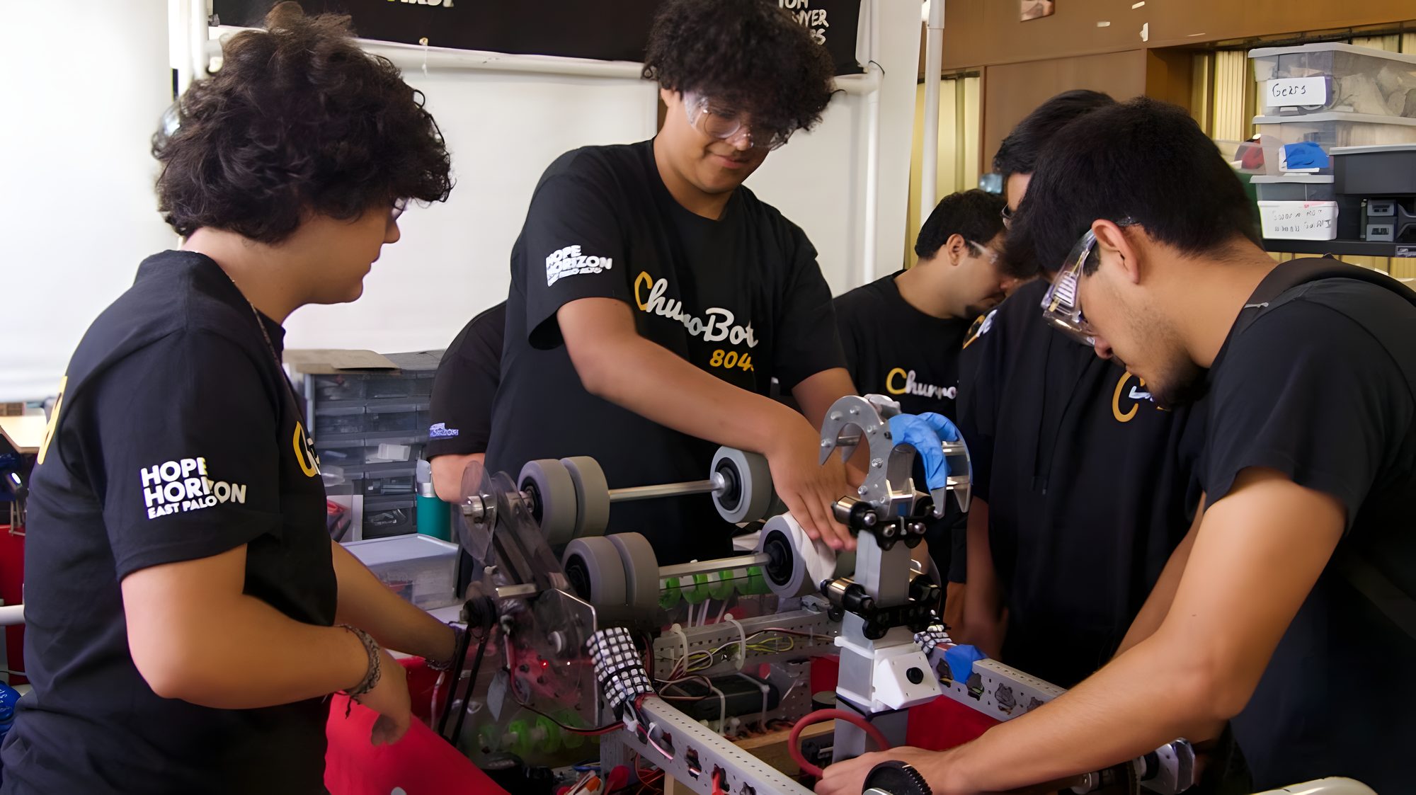 Students assemble a robot chassis with mentors looking on