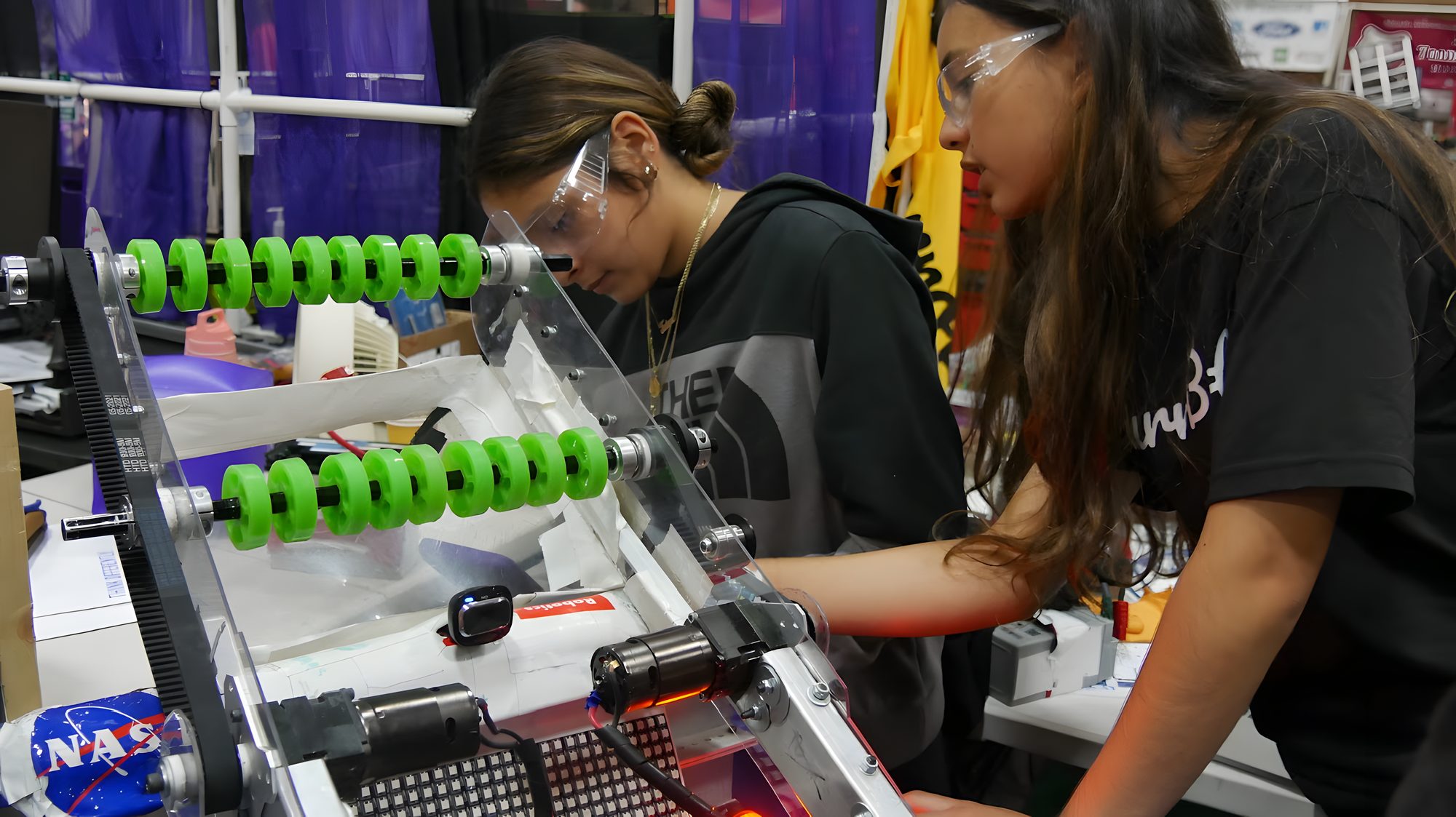 Students test a green-wheeled intake mechanism on the bench